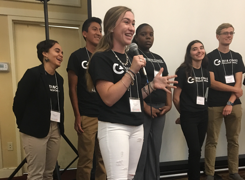 Diverse student leaders in matching t-shirts speak to teacher institute. 