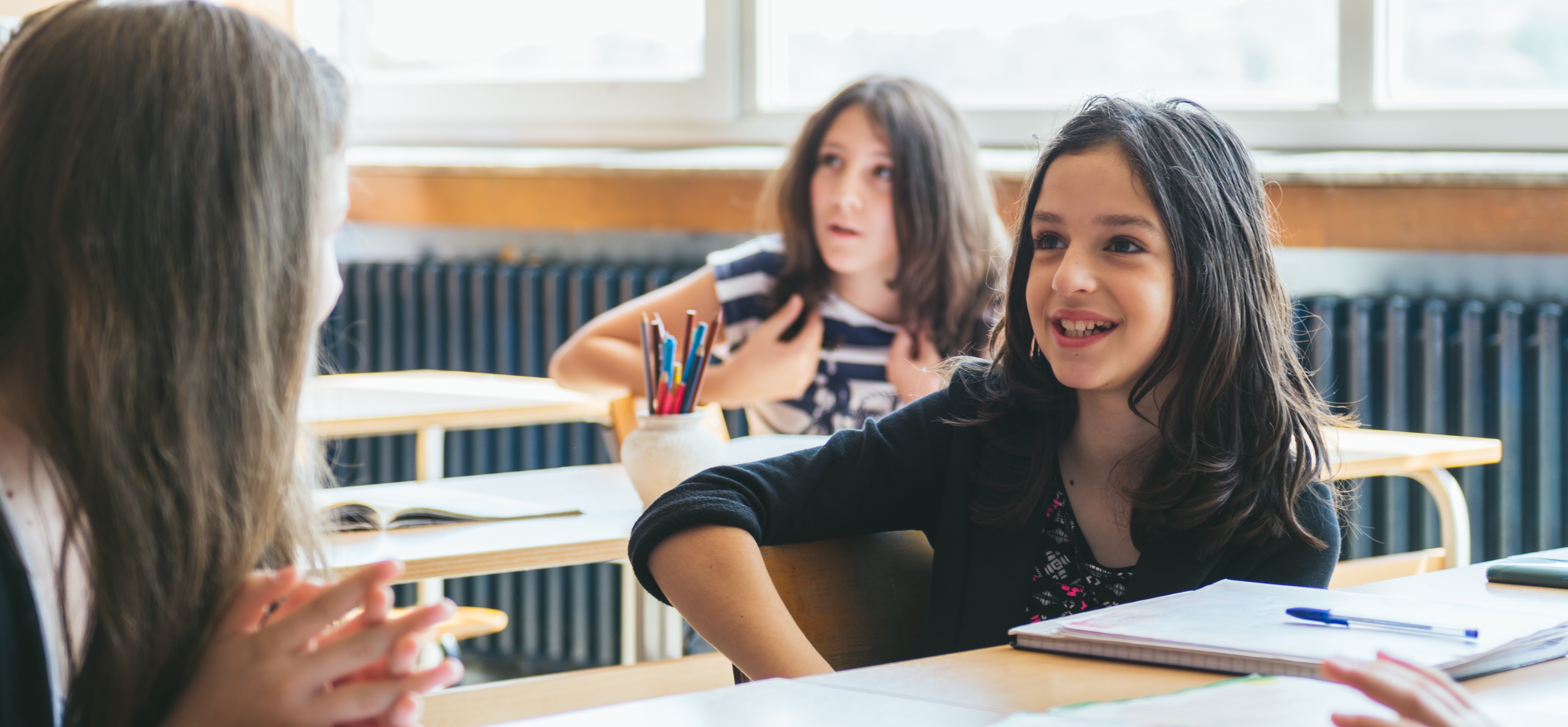 Elementary girls at classroom desks talking with animated faces