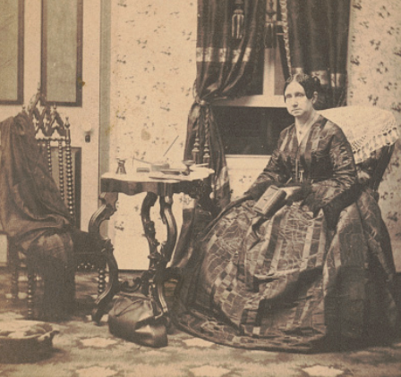 Dorothea Dix in a long dress holds a book and sits in a room with a medical bag on the floor