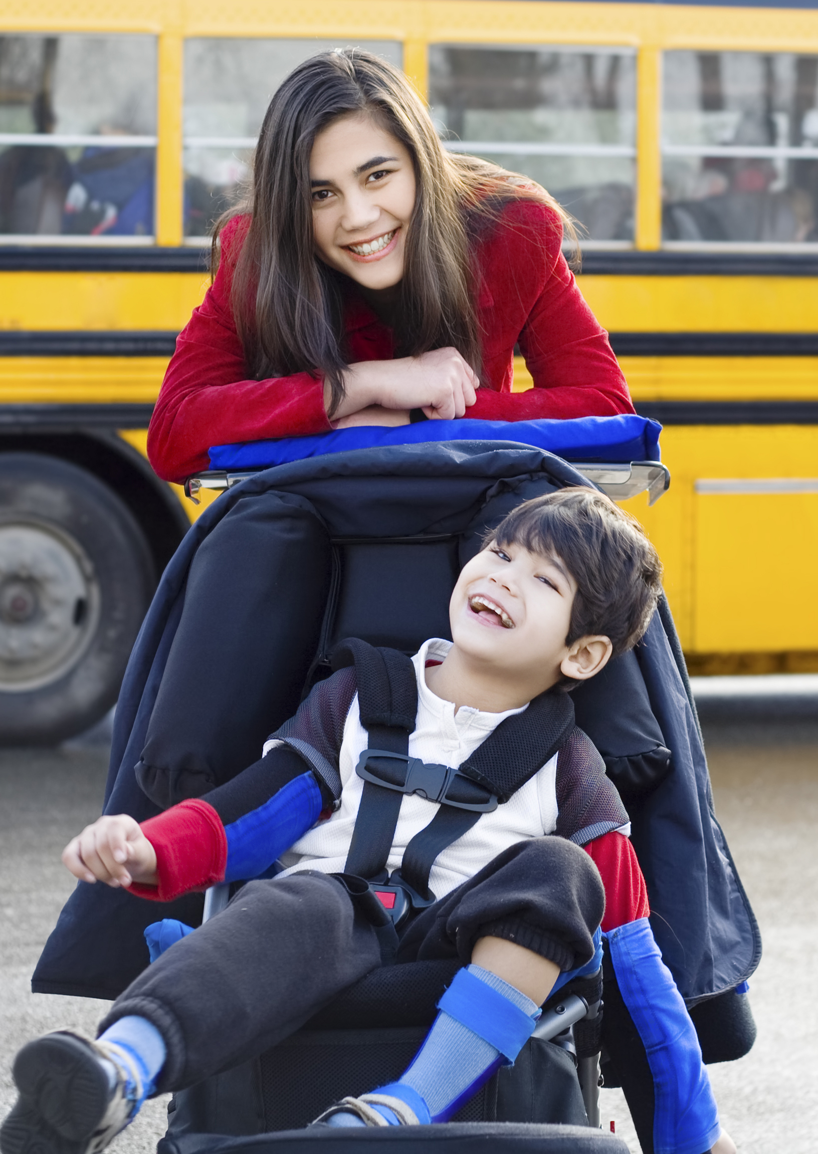 Smiling young student in wheelchair with teen by school bus. 