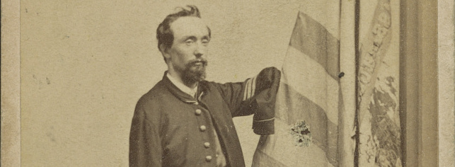 A white man with beard, wearing a Union Army jacket. His sleeves are empty. 
