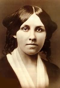 A photo of Louisa May Alcott as a young woman. Her long hair is parted in the middle and raised in wings on the side of her head. A billowy blouse shows under a sweater or jacket. She looks directly at the camera. 