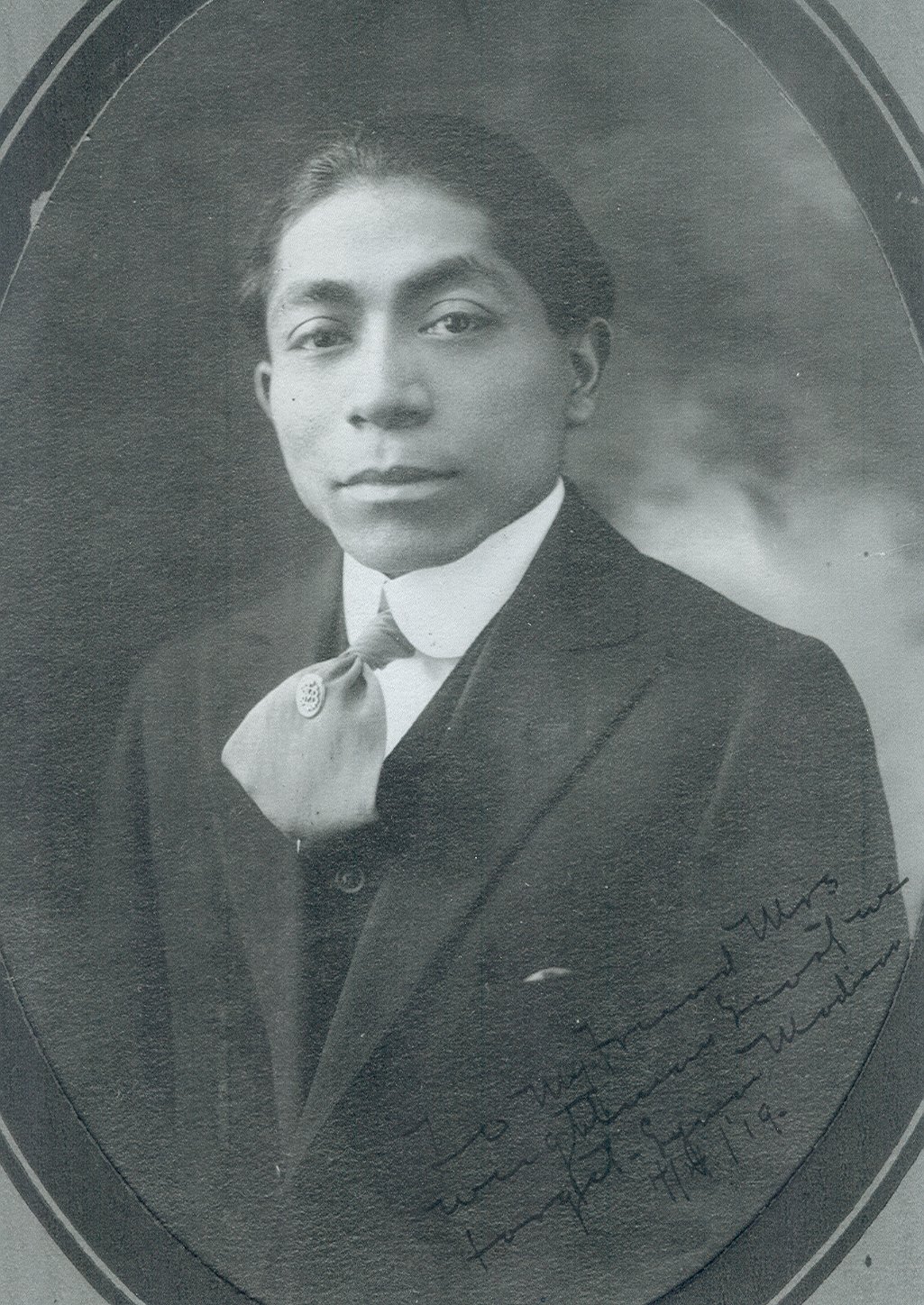 Studio portrait of Lyman Madison a Mashpee Wampanoag student at Carlisle. Madison is pictured with short black hair wearing a dark suit with a white shirt and light grey tie.