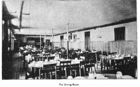 Labeled The Dining Room, a print shows a dozen tables for eight set for dinner. There are pictures on the walls. 