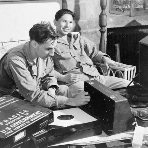 Two blind young men in uniform sit back and talk as they listen to a recording of a book
