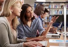 One of two teachers points at something on a computer screen as they talk. 