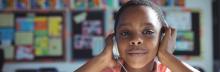 A young boy in a classroom holds his hands over his headphones. 