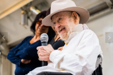 New Jersey disability activist Ethan B. Ellis speaks into a microphone - he has white beard and wears a cowboy hat 