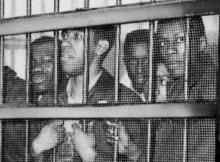 Several Black men stand behind jail bars