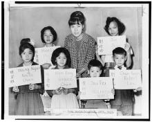 Teacher and students holding cards with their names, posing for photographer