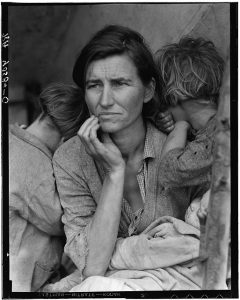 A woman with tired children leaning on each shoulder looks worried as puts her hand to her face in a black and white photo.