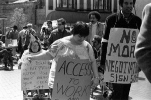 Carrying signs demanding access to work, women and men in wheelchairs and on foot march in the streets, 1977 