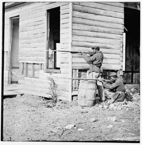 Two men with weapons standing and kneeling in position to fire. 