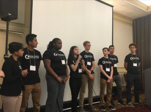 Group of students standing together on stage in front of a projector screen.