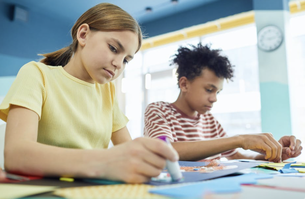 Two students, a girl and a boy, each work at a table. 