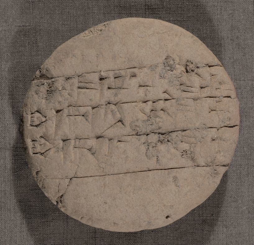 A round, clay tablet with triangular marks arranged in lines of text