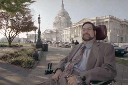 Man with a beard in a suit in a wheelchair in front of the U.S. Capitol building