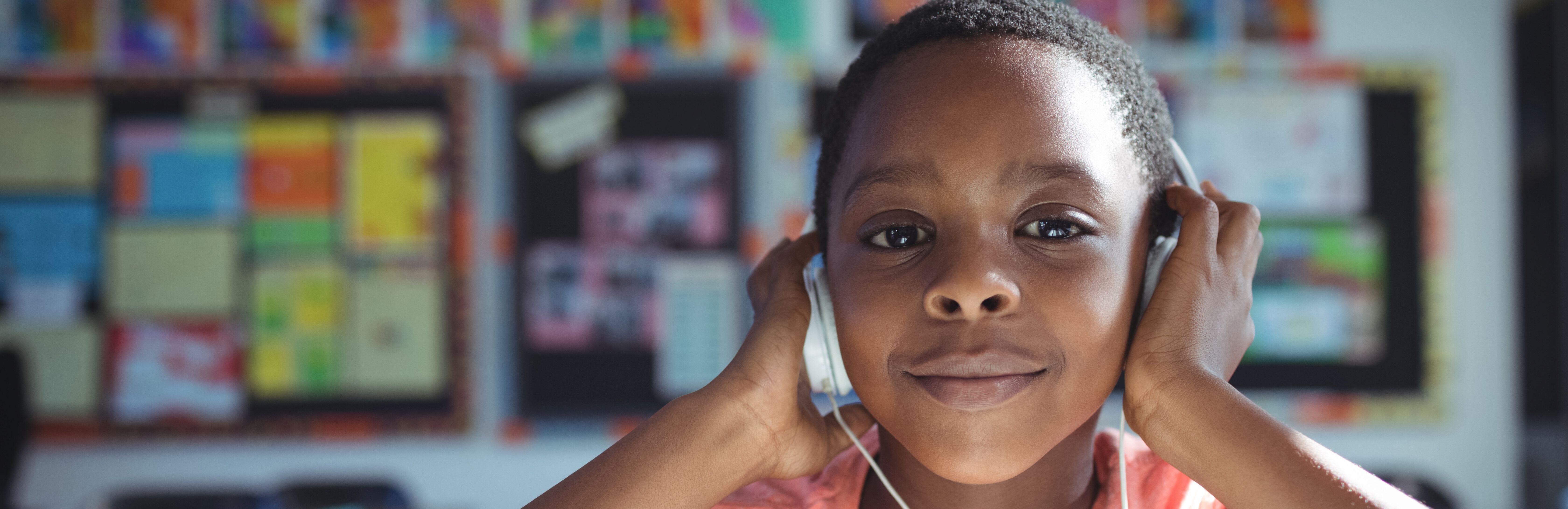 A young boy in a classroom holds his hands over his headphones. 