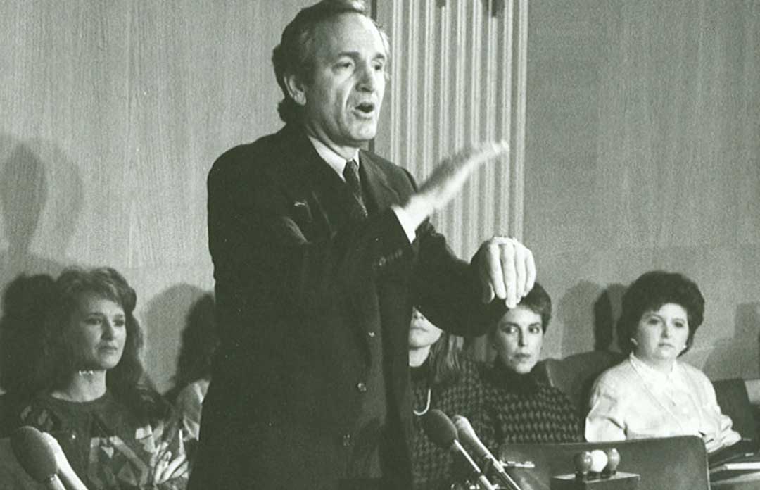 Senator Tom Harkin wearing a suit speaks passionately in American Sign Language to a group of seated women