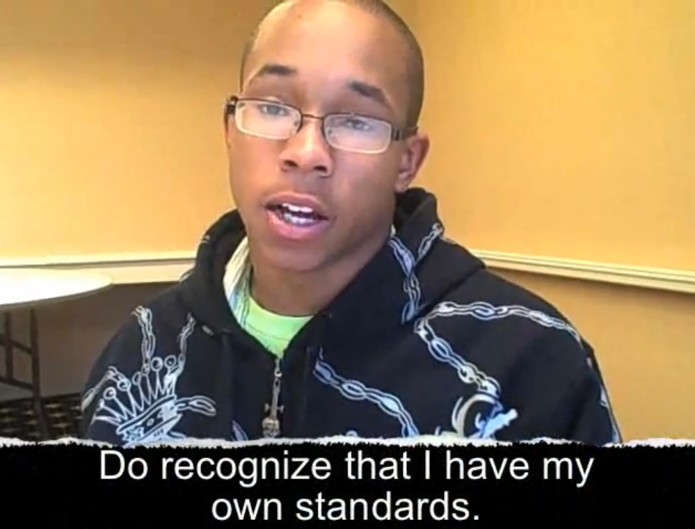 A young Black man with short hair and glasses is wearing a sweatshirt with a crown on it. A caption reads, "Do recognize that I have my own standards."