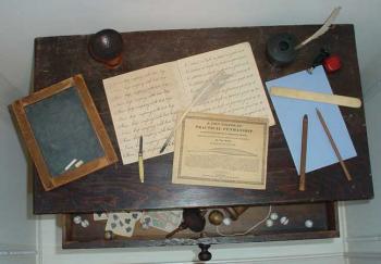 Student portable writing desk with slate, writing materials, and penmanship manual; drawer contains cards, top, and other toys.