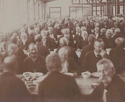 Hundreds of veterans sit at tables in a huge dining hall with high rafters.