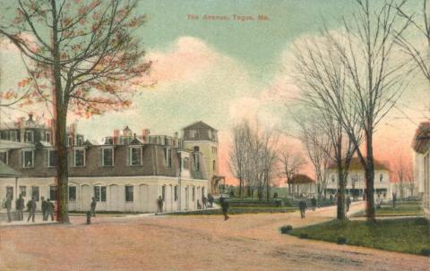 Several two-story wooden buildings cluster on a tree-lined campus. Several men walk or stand outside. 