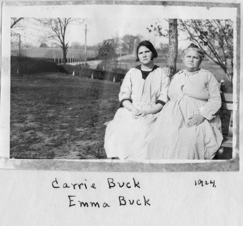 A young woman and her mother in simple dresses sit outside on a bench. 