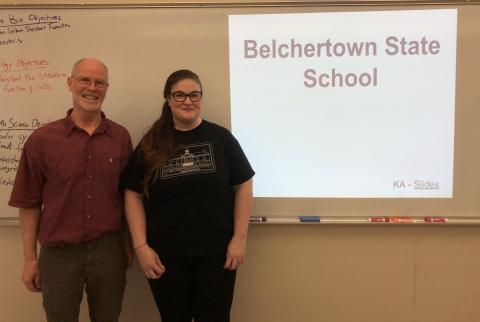 "Belchertown State School" words are projected on a classroom whiteboard beside two smiling presenters. 