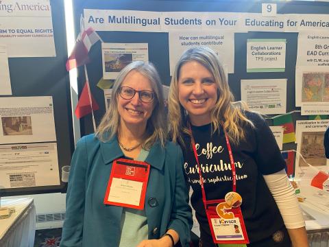 Two smiling women wearing name tags stand in front of a conference poster. 