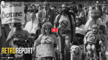 Screenshot from RetroReport film on the Disability Rights Movement shows the front of a column of disability rights marchers, including one holding a banner that reads "We Shall Overcome"