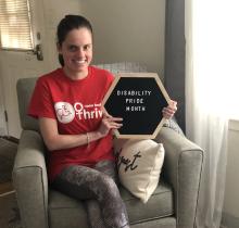 "A smiling young woman holds a sign that reads Disability Pride Month. She has a pony tail, and she wears a t-shirt reading Easter Seals Thrive.