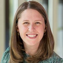 A white woman with shoulder length hair smiles at the camera